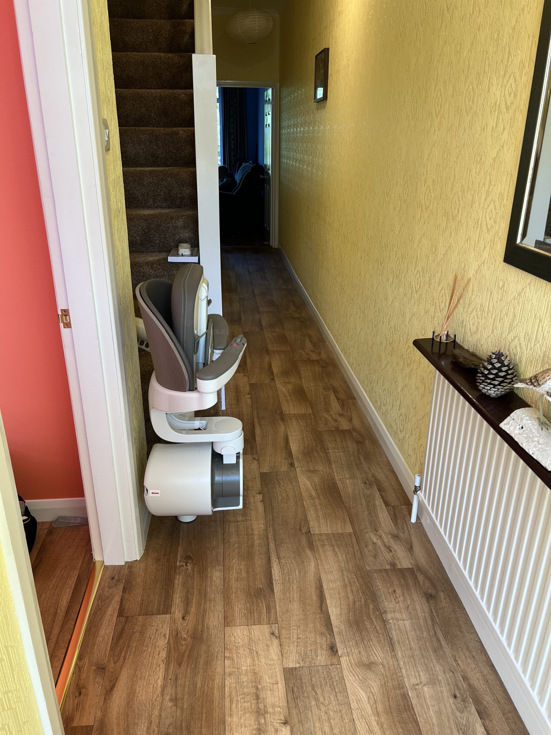 Flow X curved stairlift specialist example seat folded and parked at bottom of stairs